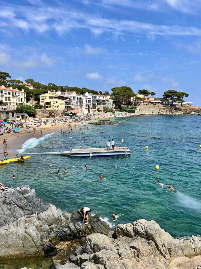 Crowded beach with clear blue water.