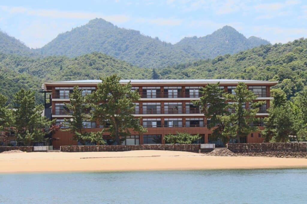 8 UNIQUE Miyajima Ryokans, Hiroshima 26 Seaside hotel with mountain backdrop.