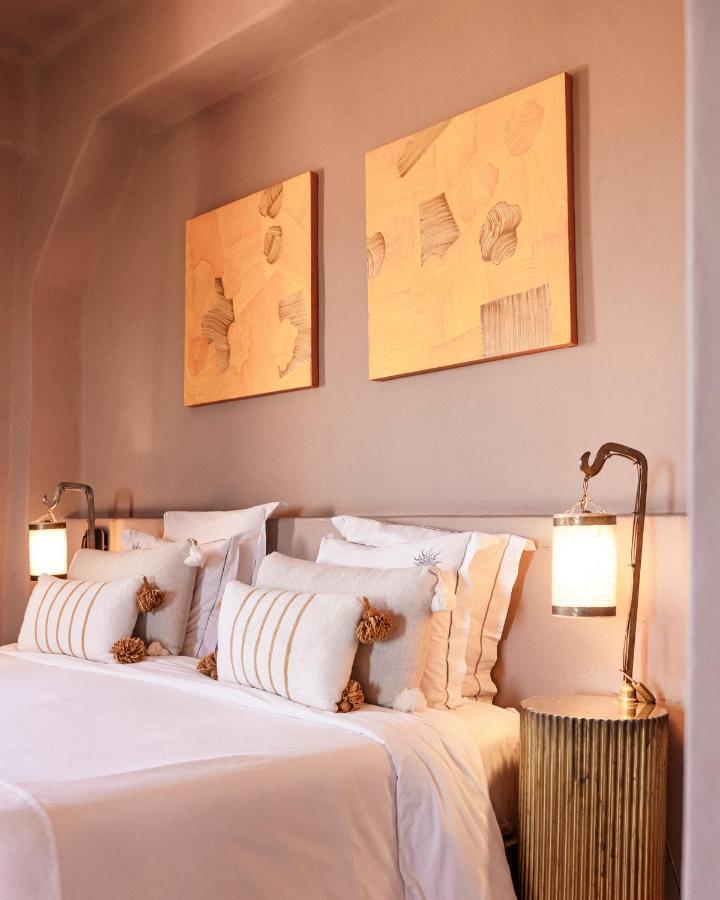 10 BEST Riads in Essaouira 49 A cozy bedroom inspired by riads in Essaouira, featuring a neatly made bed with white linens, decorative pillows, two lantern-style lights, and abstract beige artworks above the headboard.