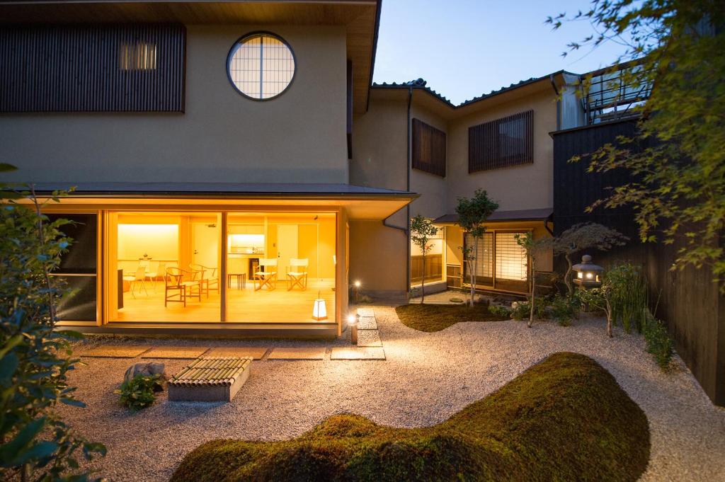 8 UNIQUE Miyajima Ryokans, Hiroshima 36 A modern Japanese-style house at dusk features large illuminated windows, a minimalist interior, and a serene rock garden with moss and raked gravel, evoking the tranquil ambiance of Miyajima ryokans.