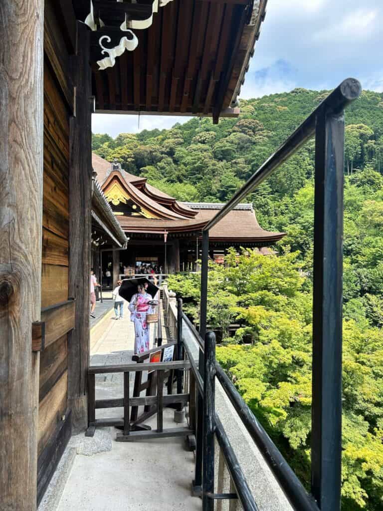 ULTIMATE 10 Day Japan Travel Itinerary 8 A person in a pink kimono stands on a wooden balcony, enjoying lush green views at a traditional Japanese temple—an inspiring scene for any 10 day Japan travel itinerary.