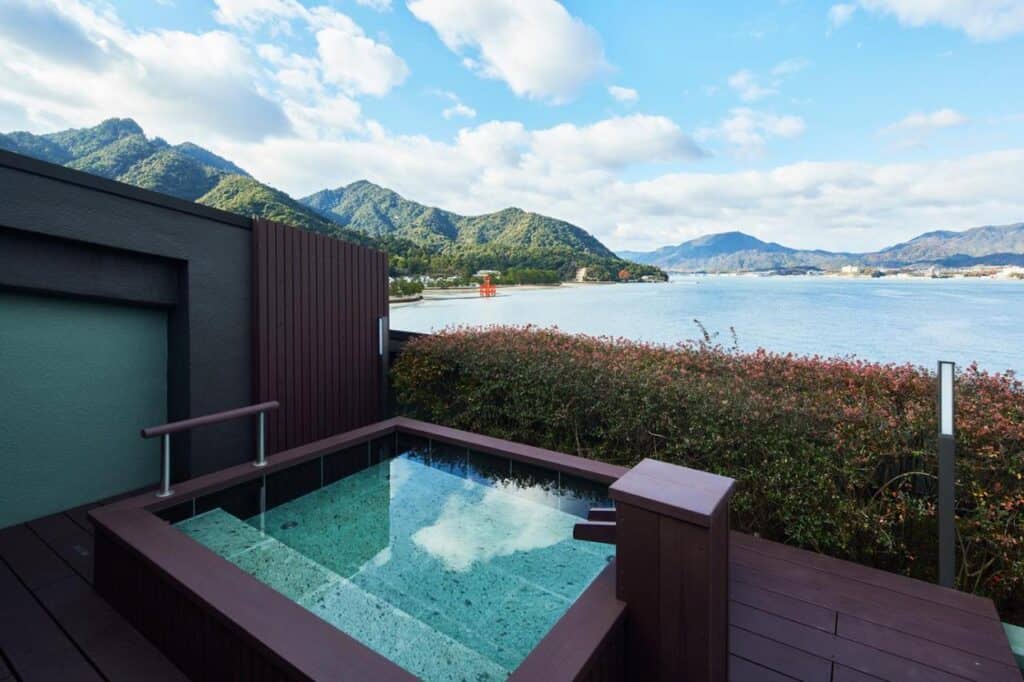 8 UNIQUE Miyajima Ryokans, Hiroshima 17 Scenic outdoor onsen with mountains.