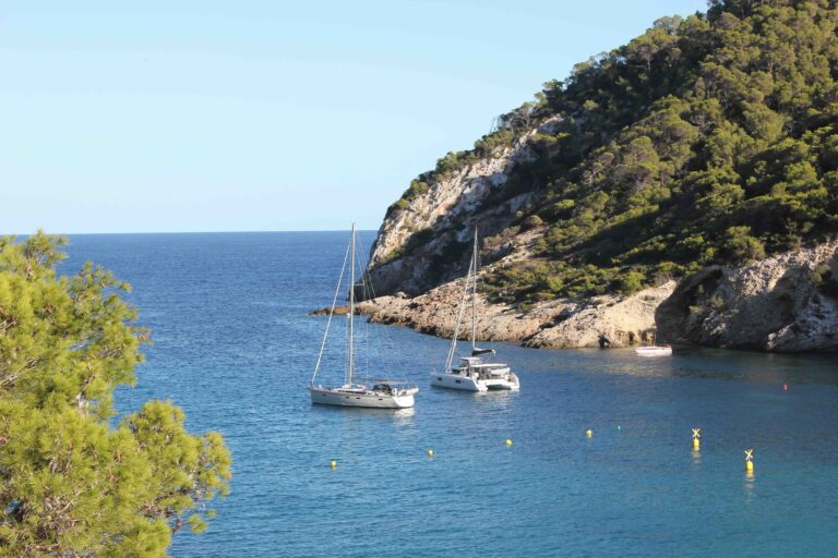A serene body of water in Ibiza, Spain, with colorful sailing boats gently bobbing on the waves.