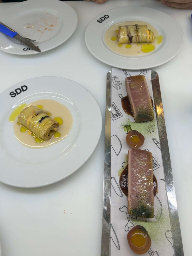 15 Most Fun Restaurants in Madrid 48 Two white plates each hold a rolled dish in pale sauce with green oil drops. Nearby, a rectangular tray displays seared tuna with sauce and garnish—an elegant presentation typical of fun restaurants in Madrid.