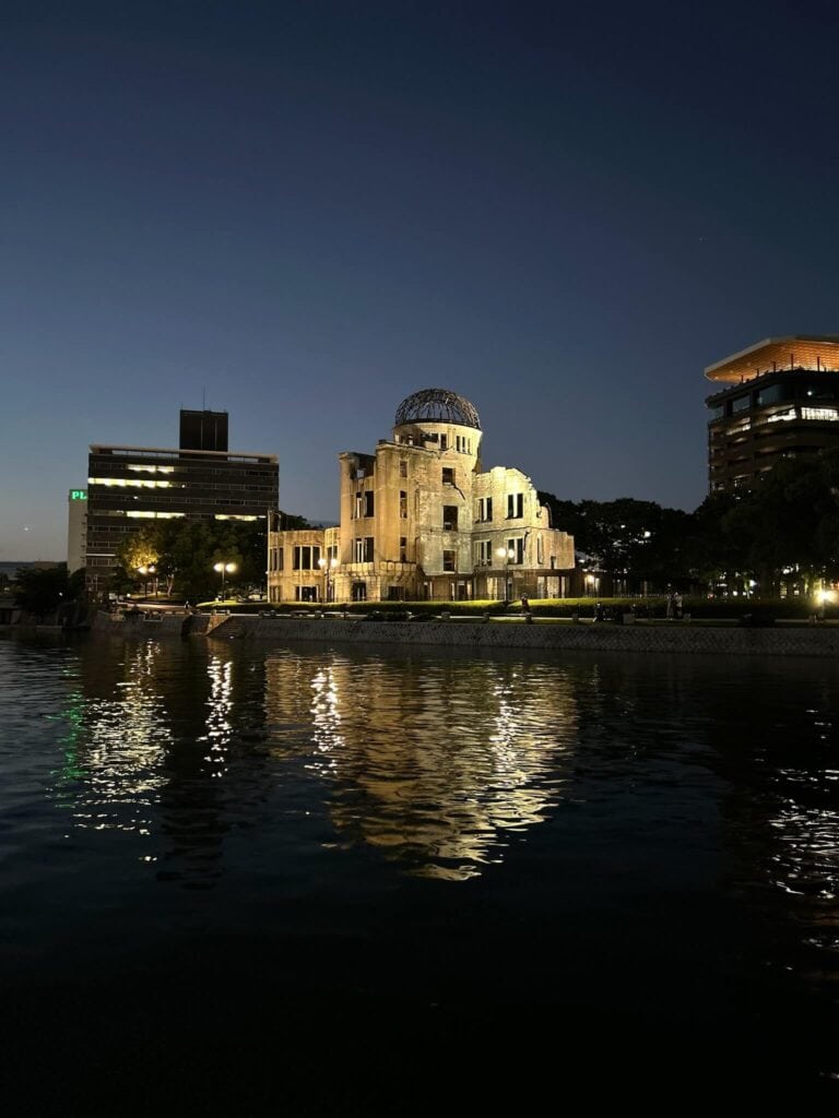 ULTIMATE 10 Day Japan Travel Itinerary 17 The Atomic Bomb Dome in Hiroshima is illuminated at dusk, reflecting in the calm river below—an unforgettable highlight on any 10 day Japan travel itinerary, with dark silhouettes of nearby buildings against the evening sky.