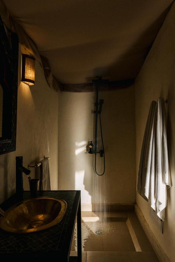 8 SPECTACULAR Agafay Desert Camps 20 A minimalist bathroom with a gold sink on a dark counter, a wall-mounted shower with running water, and two white towels evokes the cozy ambiance found in Agafay desert camps, enhanced by soft, warm lighting.