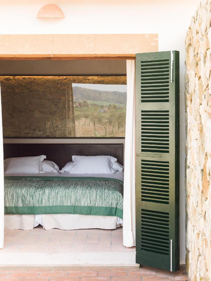 Unique Agroturismos in Mallorca 27 A cozy bedroom with a made bed, white pillows, and green bedding is seen through an open door with green shutters. The stone walls and window behind the bed reveal an outdoor rural landscape, typical of agroturismos in Mallorca.