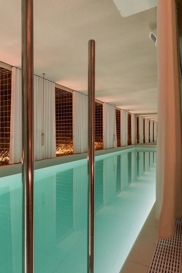Where to Stay in Madrid: 14 Best Hotels 27 Indoor swimming pool with clear turquoise water, surrounded by white walls and sheer curtains. Warm, ambient lighting reflects on the water—an inviting option for those seeking where to stay in Madrid first time. Gridded windows line the far wall.