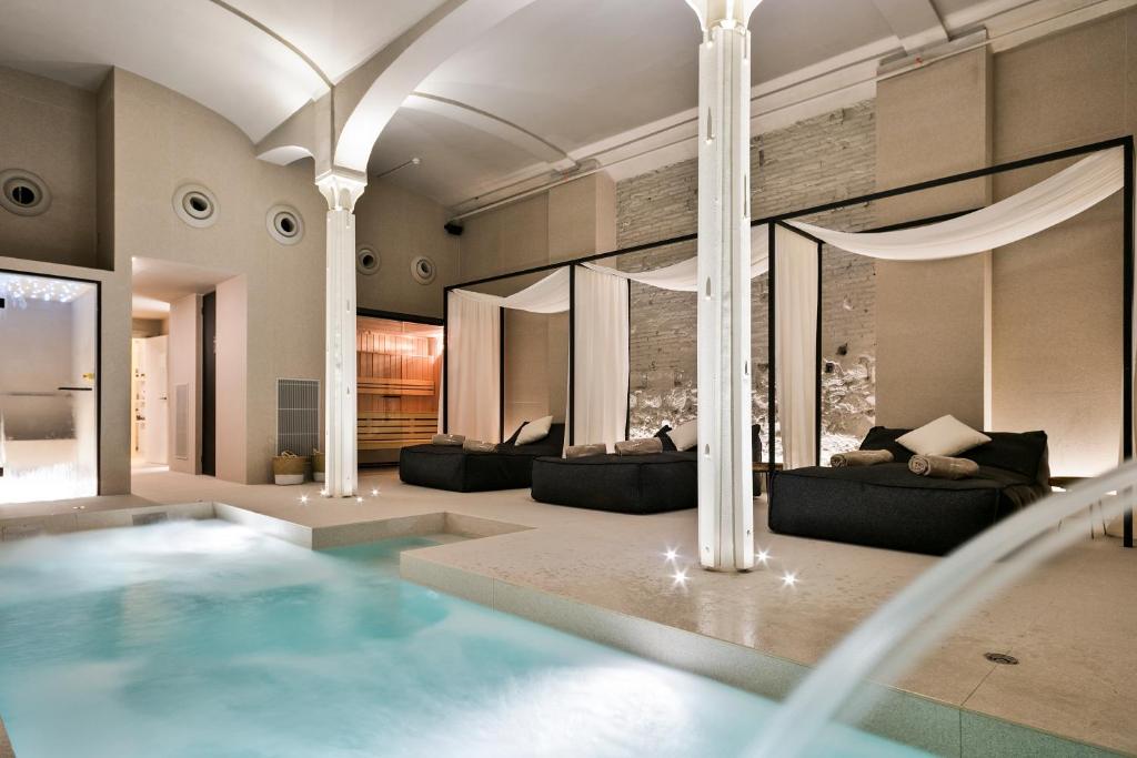 Top Barcelona Hotels with Rooftop Pool 13 A luxurious indoor spa with a small pool, elegant white pillars, draped canopy beds, and soft lighting evokes the serene atmosphere found in exclusive Barcelona hotels with rooftop pools, perfect for ultimate relaxation.