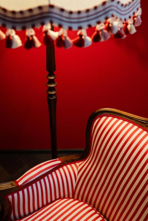 Unique Boutique Hotels in Salzburg 9 A red and white striped upholstered armchair sits next to a standing lamp with a decorative fringe shade, set against a bold red wall—evoking the stylish ambience of boutique hotels in Salzburg.