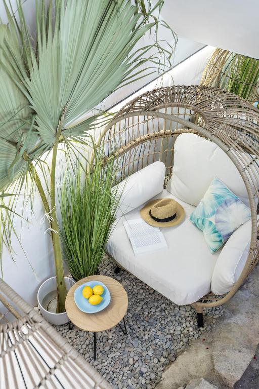 8 TOP Boutique Hotels in Split 15 A cozy outdoor lounge chair with white cushions sits under a large palm plant—evoking the relaxed vibe of Where to Stay in Split. A straw hat, open book, and colorful pillow rest on the chair, while a nearby table holds a blue bowl of lemons.