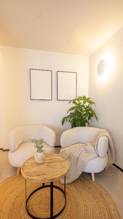 Adults-Only Hotels in Costa del Sol 7 A cozy corner with two white armchairs, a round wooden coffee table with a small potted plant—perfect inspiration for relaxing lounges in adult only hotels in Costa del Sol—plus a beige throw, leafy plant, and minimalist framed art on a white wall.