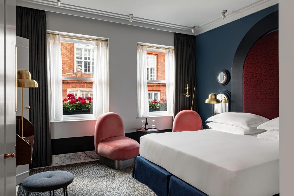 15 Best Boutique Hotels in London, UK 52 A stylish boutique hotel room in London with a large bed, two pink chairs, white walls, dark curtains, and windows overlooking red brick buildings. Modern decor and a cozy atmosphere make it perfect for a chic stay.