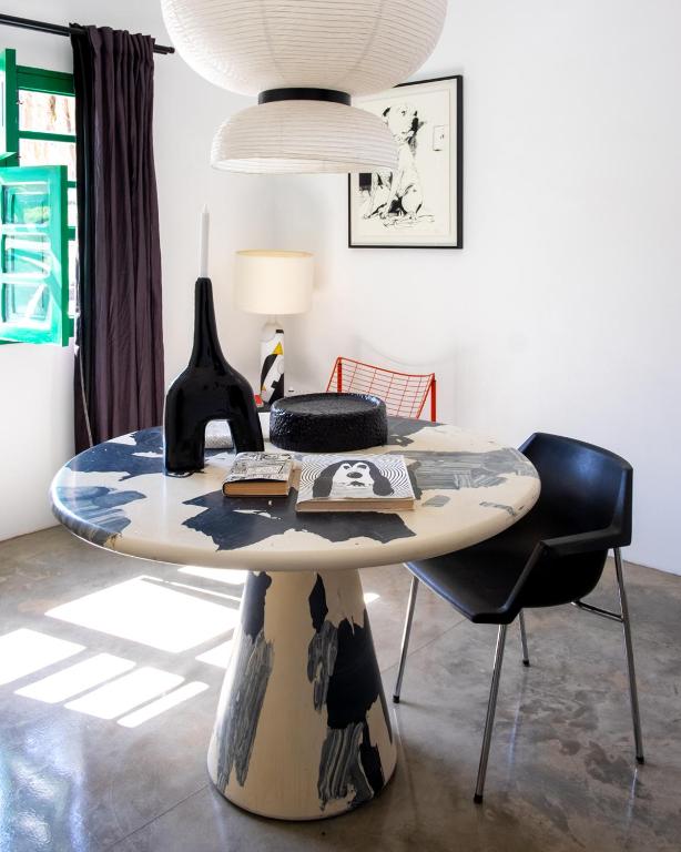 Unique Adults Only Hotels in Lanzarote 13 A modern dining area with a round, abstract-patterned table, black chair, sculptural vases, and artwork on the wall—reminiscent of the chic interiors found in Adults Only Hotels in Lanzarote. Sunlight streams through a green window onto the polished floor.