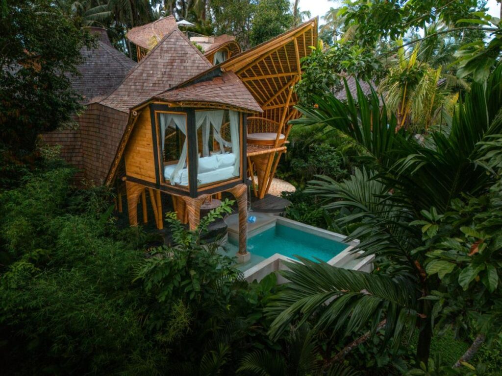 13 Most UNIQUE Places to Stay in Ubud 26 A unique bamboo villa with large windows and an open ceiling sits surrounded by lush tropical plants, overlooking a private swimming pool—a perfect choice among unique places to stay in Ubud.