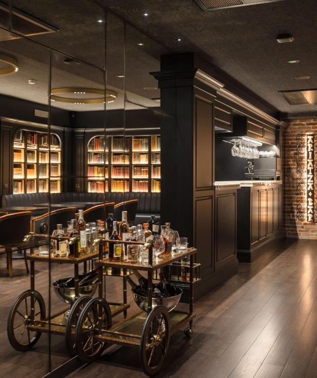8 Unique Boutique Hotels in Bilbao Spain 4 A stylish, dimly lit lounge reminiscent of boutique hotels in Bilbao, featuring dark wood floors, a mirrored wall, shelves filled with books, a bar area, and a gold drinks trolley topped with assorted bottles and decanters.