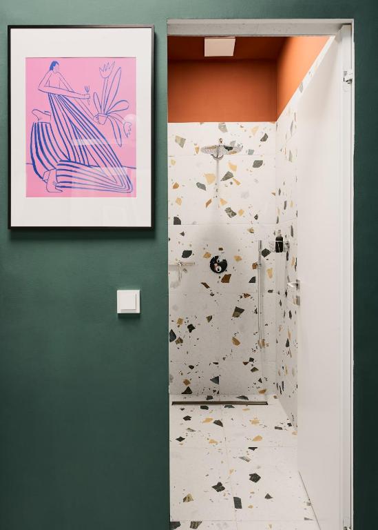 Boutique Hotels in Berlin Kreuzberg 23 A modern bathroom with terrazzo tile walls and floors, an orange ceiling, and a green wall outsideālike something from boutique hotels in Berlin Kreuzberg. A pink abstract art piece in a black frame hangs next to the doorway.