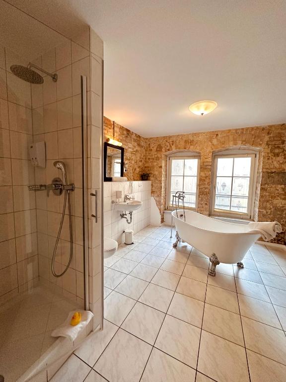 Boutique Hotels in Berlin Kreuzberg 29 A spacious bathroom with tiled floors, a glass shower, a clawfoot bathtub, and large windows letting in natural lightājust like those found in boutique hotels in Berlin Kreuzberg. Exposed brick walls add charm; a yellow rubber duck sits on the shower floor.