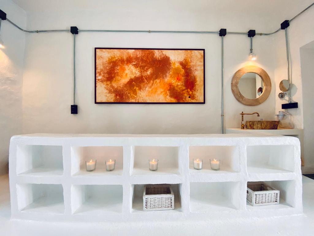 Unique Adults Only Hotels in Lanzarote 24 A minimalist white counter with built-in shelves holds candles and wicker baskets, evoking the serene style found in Adults Only Hotels in Lanzarote. An abstract orange painting and round mirror hang above a brass sink in this bright, modern setting.