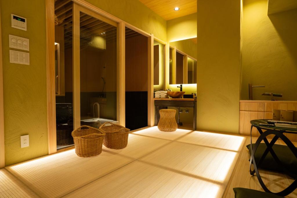 8 BEST Ryokans in Osaka 5 A serene Japanese-style room with tatami mat flooring, wicker baskets, a wooden vanity with a mirror, soft lighting, and a separate bathing area through glass doors—capturing the tranquil ambiance found in ryokans in Osaka.