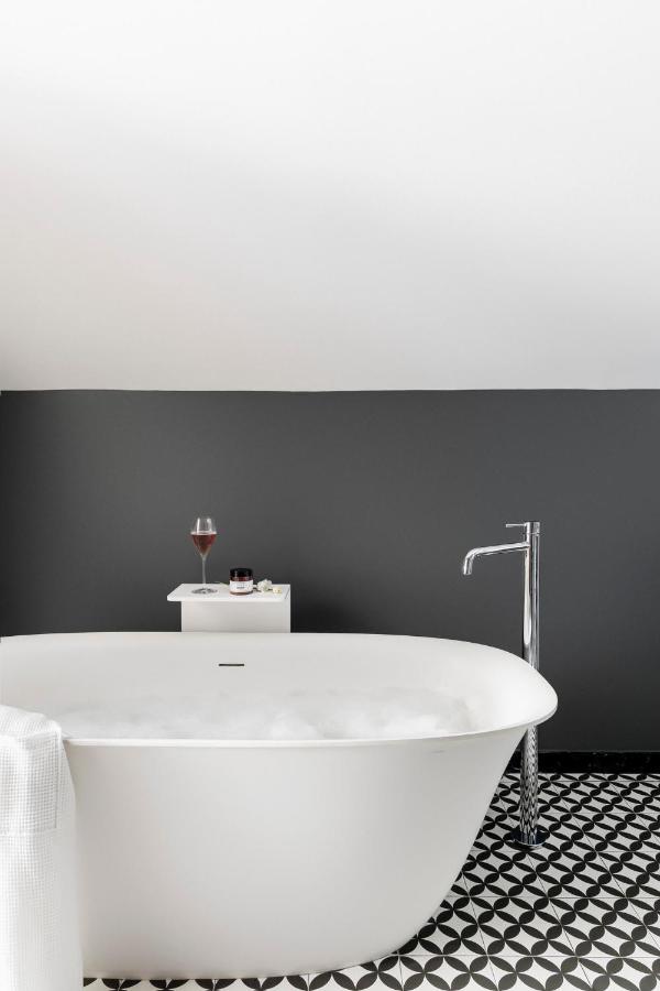 Where to Stay in Madrid: 14 Best Hotels 53 A modern bathroom—perfect for unwinding after exploring where to stay in Madrid first time—features a white freestanding bathtub with bubbles, chrome faucet, cozy towel, and a table with red wine, candle, and toiletries against a dark gray wall.