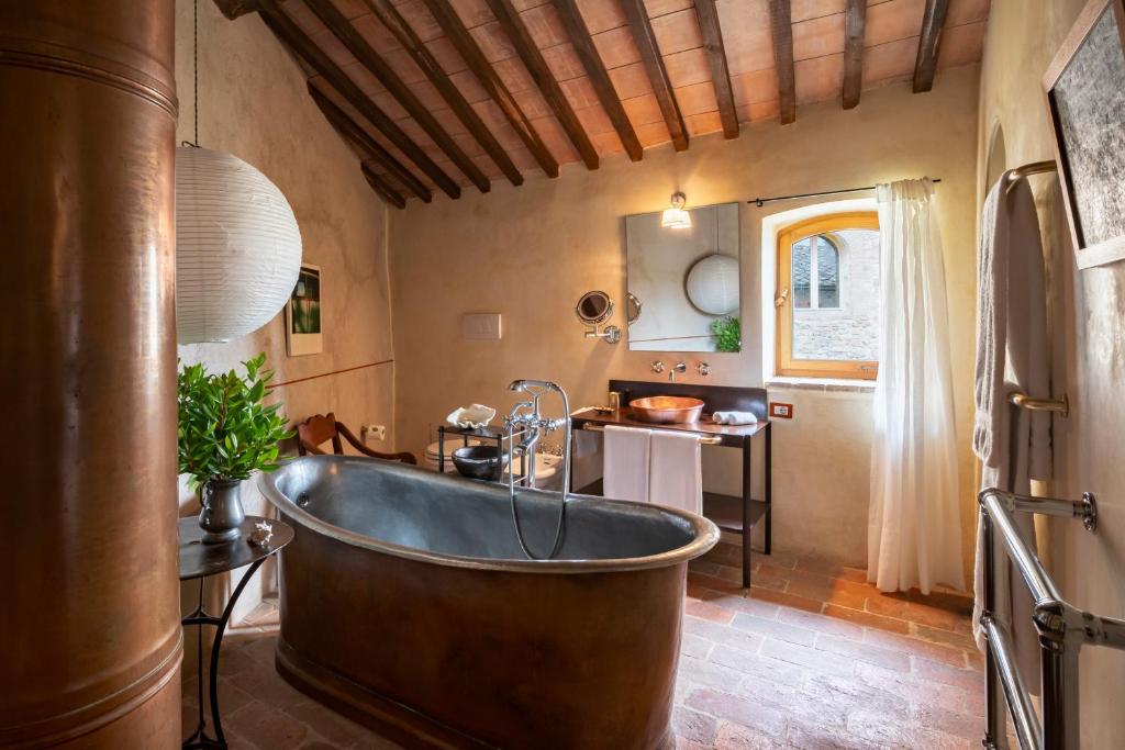 7 Best Agriturismos in Tuscany 20 Rustic bathroom reminiscent of agriturismos in Tuscany, with a copper bathtub, brick floor, wooden beamed ceiling, paper lantern, copper sink vanity, potted plant, and a window with white curtains. Warm and cozy ambiance.
