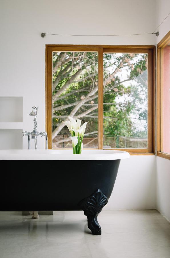 8 UNIQUE Places Where to Stay in Lake Atitlán 9 A black clawfoot bathtub with a bouquet of white calla lilies on the edge sits in a bright bathroom with a large window overlooking green trees, evoking the tranquility you'd find when searching where to stay in Lake Atitlan.