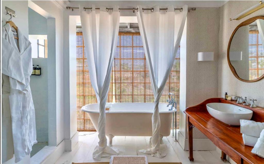 Adults-Only Hotels in Costa del Sol 18 A bright bathroom at one of the top adult only hotels in Costa del Sol, featuring a freestanding bathtub by tall windows with bamboo shades, a wooden vanity with vessel sink and mirror, and a hanging white robe on the left.