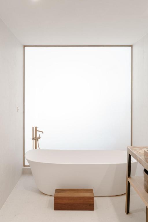 Most Unique Boutique Hotels in Dubrovnik 3 Minimalist bathroom inspired by boutique hotels in Dubrovnik, featuring a white freestanding bathtub, modern faucet, small wooden step, and a large frosted window that fills the space with soft natural light.