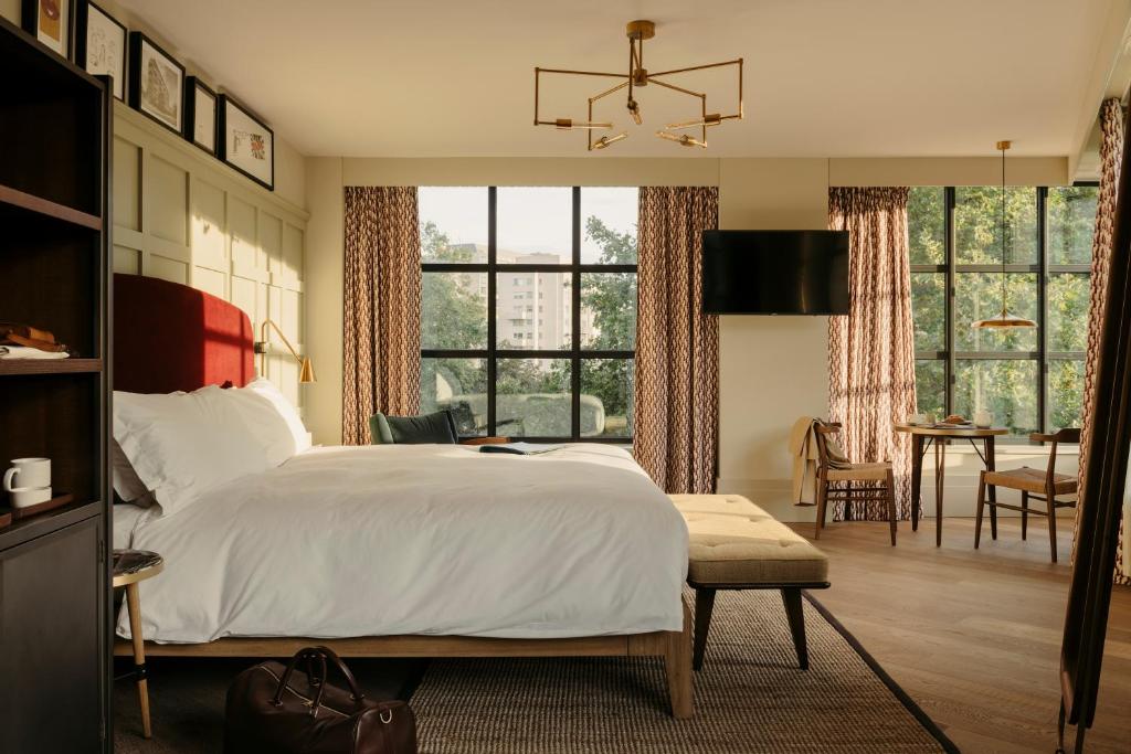 15 Best Boutique Hotels in London, UK 61 A stylish hotel room in one of the top boutique hotels in London, featuring a large bed, modern lighting, wall-mounted TV, floor-to-ceiling windows with patterned curtains, a cozy table with chairs, and warm natural light streaming in.