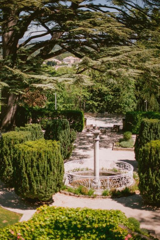 11 Unique Places to Stay in Provence 17 A lush garden with neatly trimmed hedges, a white circular railing surrounding a sundial, and benches under a large tree’s shade—sunlight filters through the leaves, creating a peaceful atmosphere often found at unique places to stay in Provence.