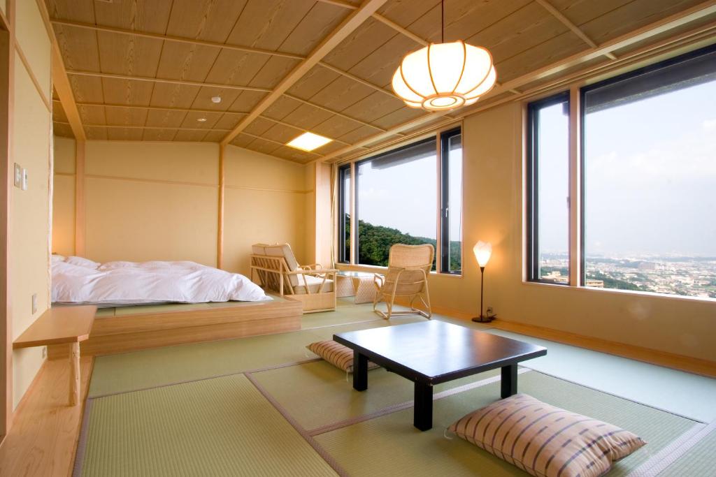 8 BEST Ryokans in Osaka 29 A bright Japanese-style room inspired by ryokans in Osaka, featuring tatami mats, a low table with floor cushions, a platform bed with white bedding, wooden chairs, large windows, and city and greenery views.
