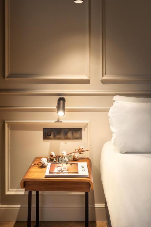 8 Unique Boutique Hotels in Bilbao Spain 10 A wooden bedside table with a magazine and a decorative branch sits next to a bed with white bedding— reminiscent of the elegant style found in boutique hotels in Bilbao; a reading light is mounted on the paneled wall above the table.