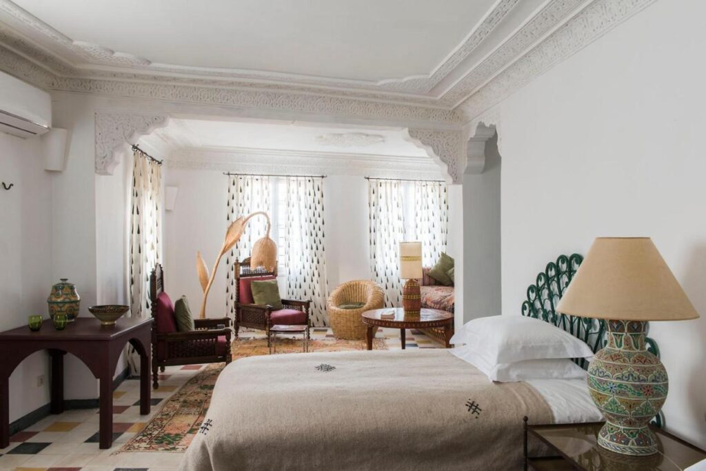 7 UNIQUE Riads in Fez You Won't Forget 12 A spacious, elegantly decorated bedroom with intricate white plasterwork, a large bed, woven chairs, and traditional pottery—reflecting the charm of riads in Fez through its blend of Moroccan and contemporary design elements.