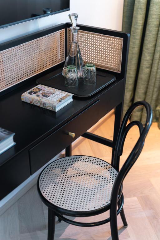 Unique Boutique Hotels in Salzburg 7 A black desk with a cane chair, featuring woven rattan details, sits beneath a TV with green curtains in the background—evoking the chic style often found in boutique hotels in Salzburg. A tray with a decanter, glasses, and a book completes the scene.