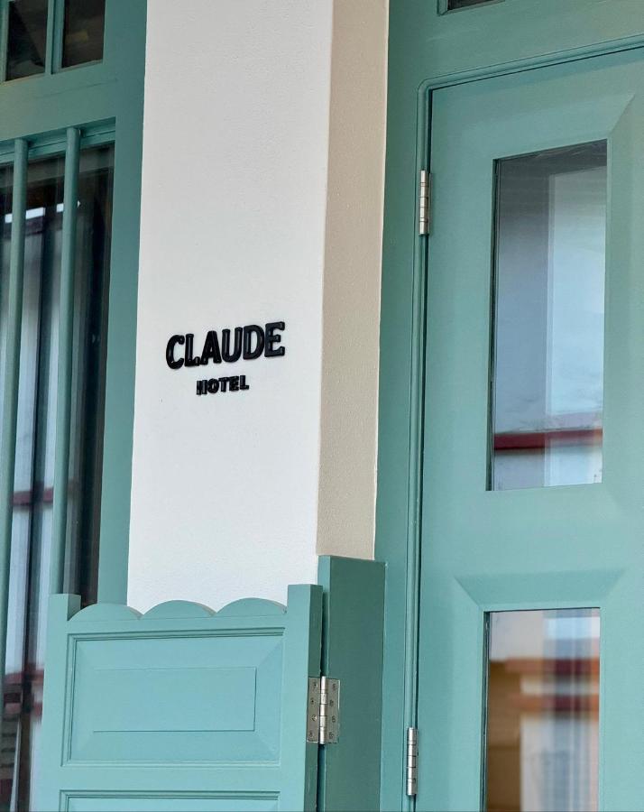 13 Most Unique Hotels in Singapore for an Incredible Holiday 24 A mint green door and half-gate beside a white wall with “CLAUDE HOTEL” in black text—one of the unique hotels in Singapore. Vertical bars and window glass are visible on the left side.