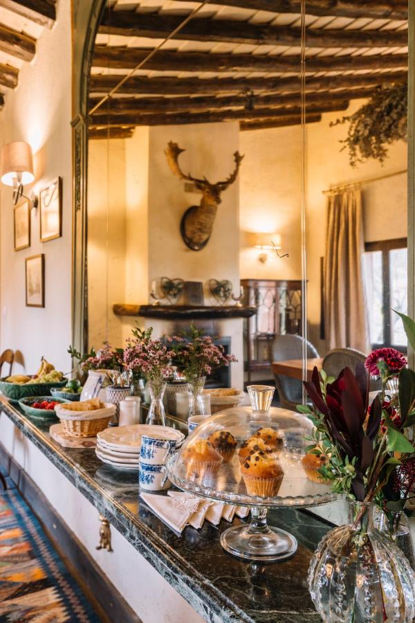 25 Weekend Trips from Madrid Max. 2h Away 48 A rustic dining room, perfect inspiration for weekend trips from Madrid, features a large mirror, set table with pastries, fruit, and flowers. Wooden beams line the ceiling and a mounted deer head decorates the cream-colored wall by a fireplace.
