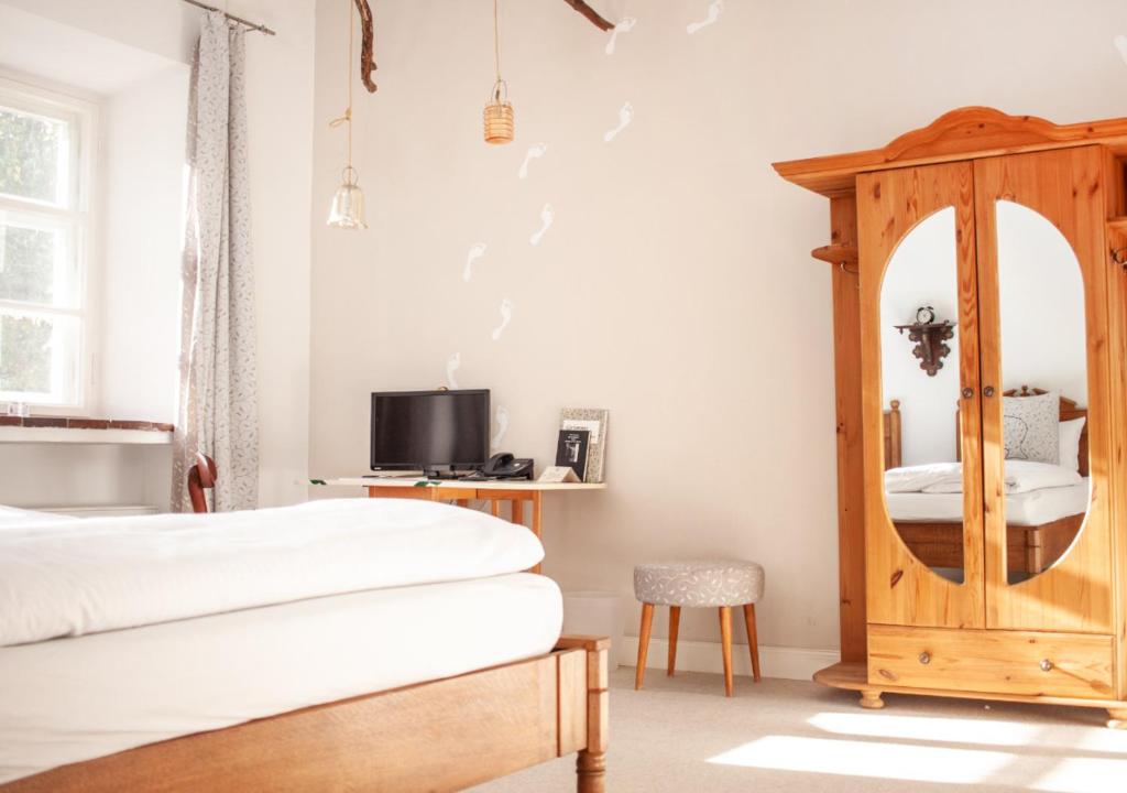 FAIRYTALE Castle Hotels in Bavaria 26 Bright, cozy bedroom reminiscent of castle hotels in Bavaria, featuring a wooden bed, mirrored wardrobe, bedside table with a small TV and photo frame, and a cushioned stool. Sunlight streams through sheer curtains, creating a warm atmosphere.