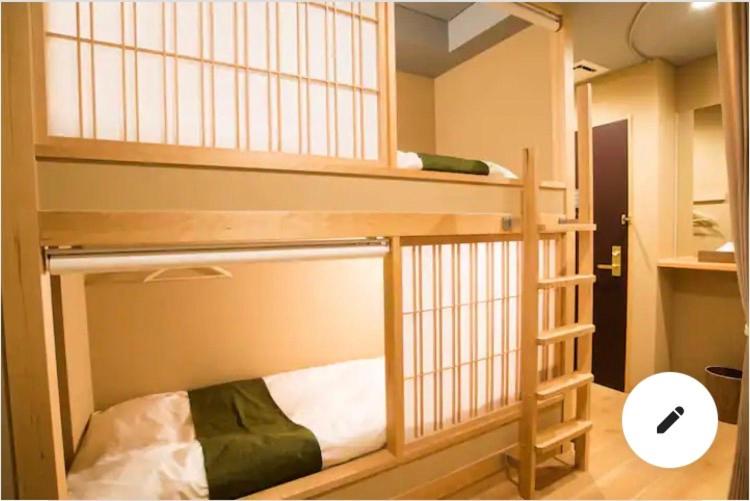 8 BEST Ryokans in Osaka 17 A cozy room inspired by ryokans in Osaka, featuring wooden bunk beds with sliding paper panel doors, white bedding, and green blankets. A small ladder leads to the top bunk amid warm lighting and minimalist decor.