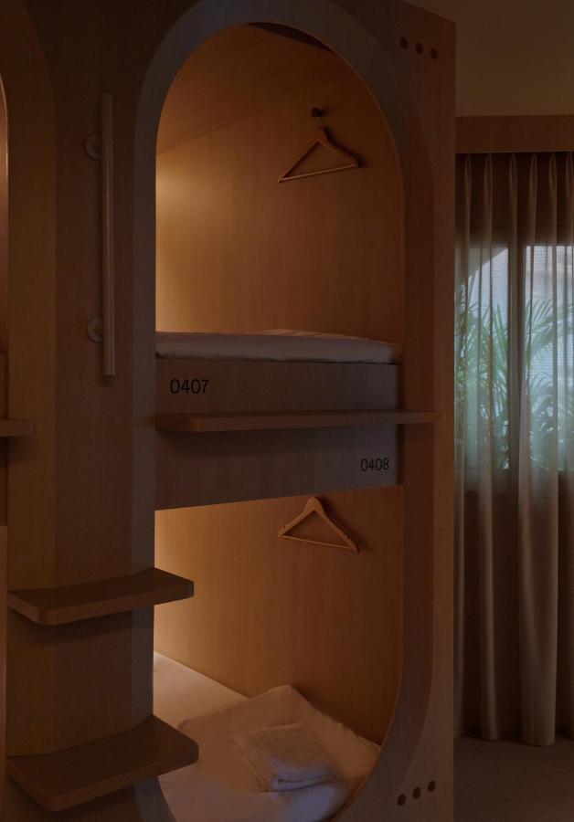 13 Most Unique Hotels in Singapore for an Incredible Holiday 38 Two capsule-style bunk beds with wooden frames, each with a hanger and bedding, are stacked vertically. Light shines softly inside each capsule, in this cozy space at one of the unique hotels in Singapore, with a window and curtains beside the beds.