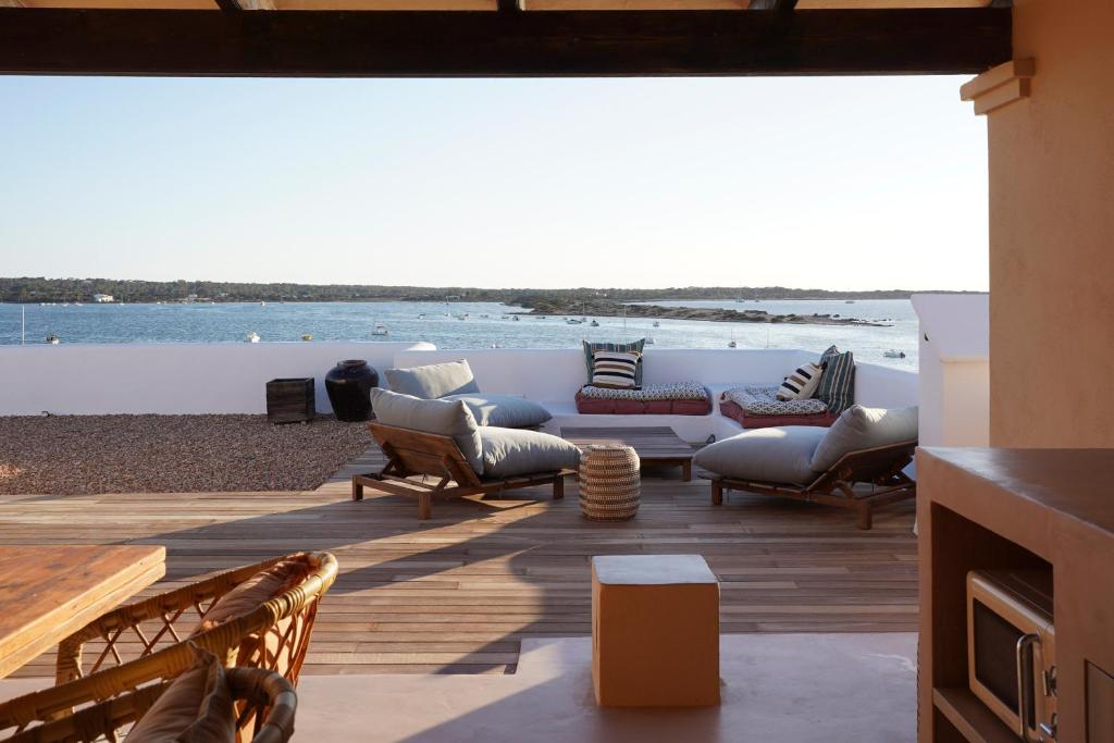 Outdoor lounge area with cushioned chairs and sofas on a wooden deck, overlooking calm water and a distant shoreline under a clear sky—reminiscent of the serene settings found at boutique hotels in Formentera.