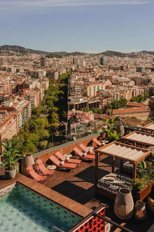 Top Barcelona Hotels with Rooftop Pool 40 Rooftop pool with lounge chairs and cabanas overlooking a cityscape, tree-lined streets, and distant hills—discover why Barcelona Hotels with Rooftop Pool are the perfect spot to unwind under a clear sky.