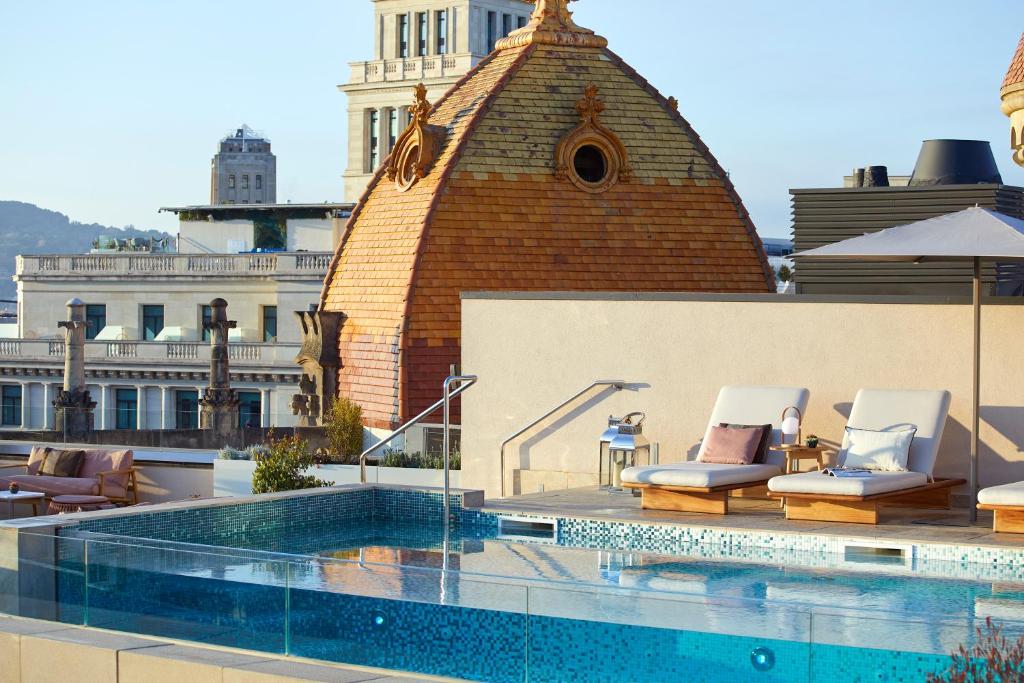 Top Barcelona Hotels with Rooftop Pool 26 Rooftop pool with clear blue water, lounge chairs, and an umbrella, set against ornate domed rooftops and historic city buildings—perfect for those seeking the charm of Barcelona Hotels with Rooftop Pool.