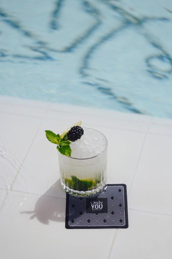 10 UNIQUE Hotels with Pool in Seville 26 A glass of cocktail with mint leaves, crushed ice, a blackberry, and a lime wedge sits on a black and white geometric coaster by the edge of a swimming pool at one of the stylish hotels with pool in Seville.