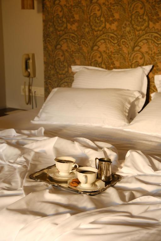 11 Unique Hotels in Georgia You Can't Miss! 22 A silver tray with two cups of coffee, a small milk jug, and a biscuit sits on a rumpled white bed in a cozy, warmly-lit bedroomājust one of the charming details found in unique hotels in Georgia.