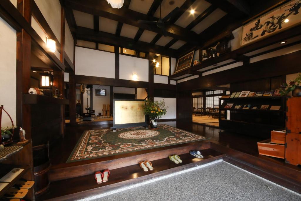 Looking for the Best Ryokan in Takayama? 4 A traditional Japanese entryway reminiscent of the Best Ryokan in Takayama, featuring wooden beams, a decorative rug, fresh flowers, and neatly placed slippers. Shelves lined with books and artwork complete the welcoming atmosphere.