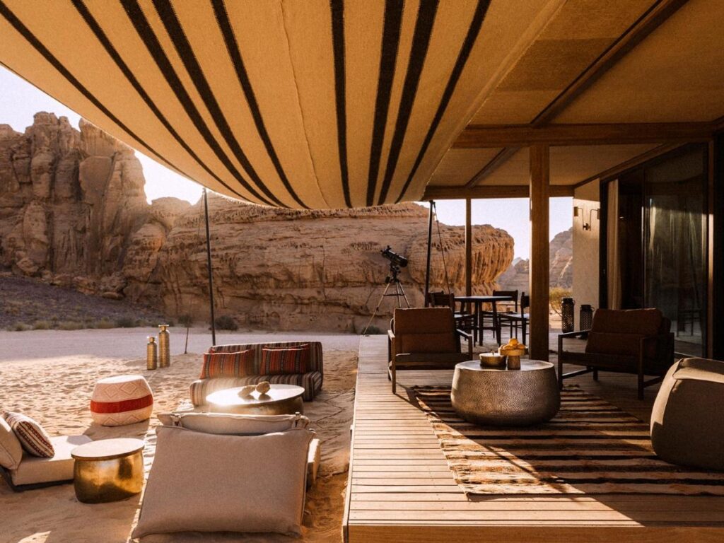 9 Best Hotels in Saudi Arabia: Unique Stays Across the Country 13 Desert glamping setup with a shaded wooden deck, modern lounge chairs, patterned cushions, and a telescope facing rocky formations—an experience inspired by the luxury of the Best Hotels in Saudi Arabia.