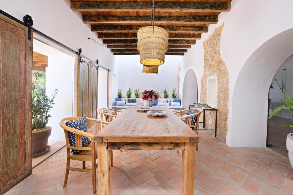 A rustic dining area with a wooden table and chairs, potted plants, exposed wooden beams, arched doorways, stone walls, and cozy blue-cushioned seating—reminiscent of the relaxed charm found in boutique hotels in Formentera.