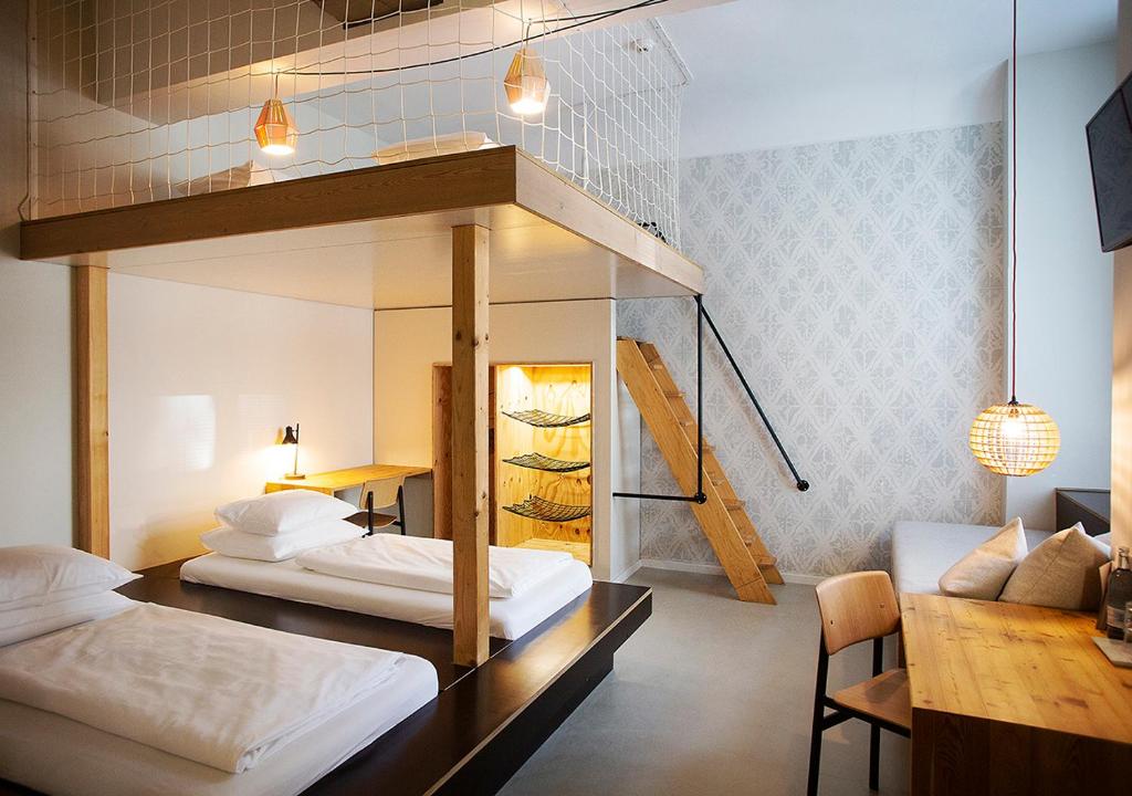 Boutique Hotels in Berlin Kreuzberg 9 Modern, minimalist bedroom inspired by boutique hotels in Berlin Kreuzberg, featuring two single beds, a wooden loft with stairs, a desk and chairs, ambient lighting, patterned wallpaper on one wall, and a net safety railing for the loft area.