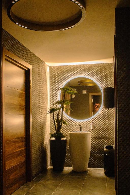 8 Unique Boutique Hotels in Bilbao Spain 5 A modern bathroom with textured walls, a round backlit mirror above a sleek white pedestal sink, a tall potted plant, and soft warm lighting—reminiscent of the style found in boutique hotels in Bilbao.